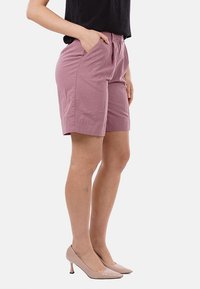 Shorts di cotone rosa con una vestibilità relaxed, tasche laterali e una texture sottile, abbinati a scarpe con tacco alto di un beige chiaro.