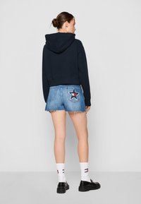 Felpa cropped navy abbinata a pantaloni shorts in denim blu con una toppa a stella sul retro, orli sfilacciati e scarpe con tacco block nere.