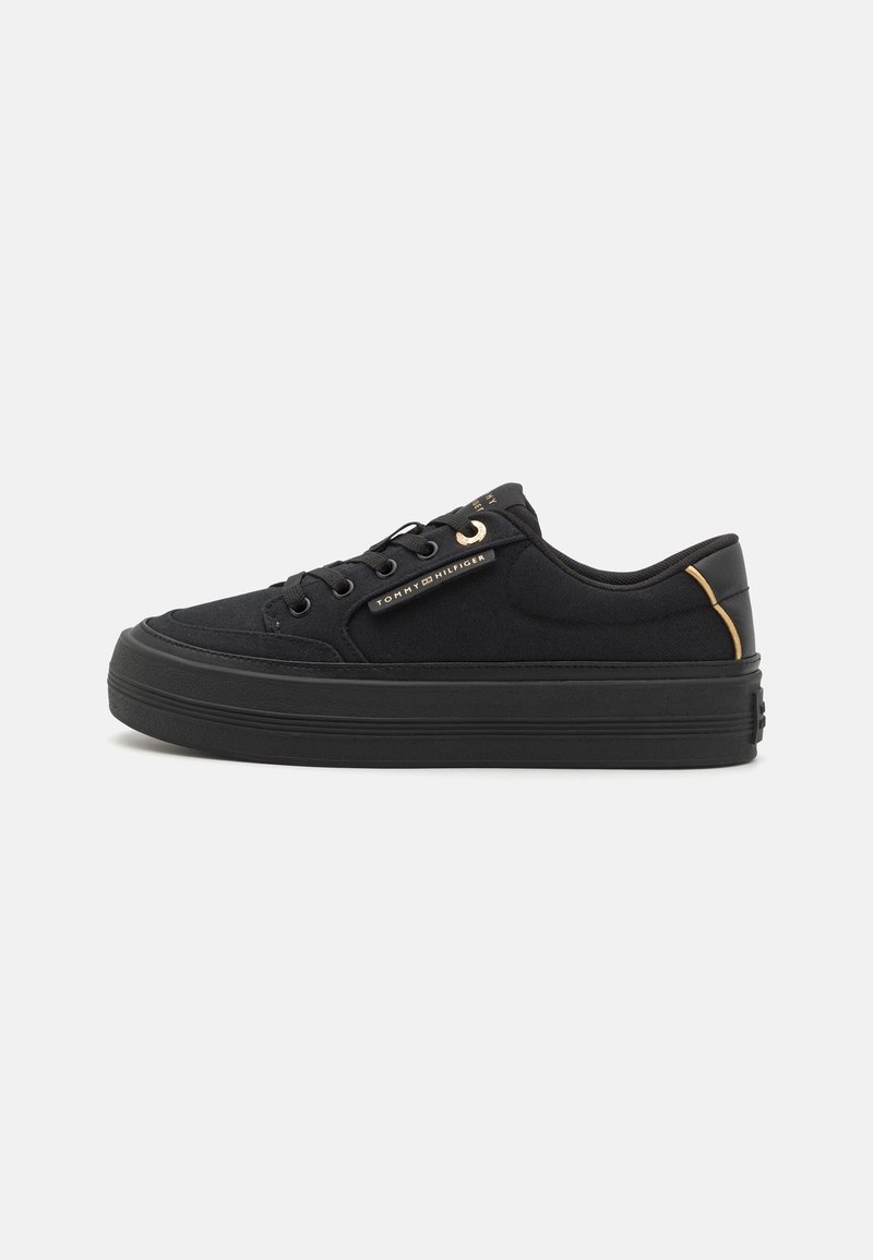 Basket basse noire avec semelle épaisse, design à lacets, petit accent doré et logo Tommy Hilfiger sur le côté et la languette.