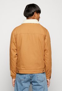Tan denim jack met een faux shearling kraag, knoopmanchetten en zijzakken. Beschikt over een eenvoudig ontwerp met zichtbare stikdetails.