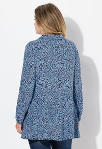 Dlouhá modrá blůza s černým a růžovým leopardím potiskem, s límečkem a rozšířeným lemem. Hladká tkanina a uvolněný střih.