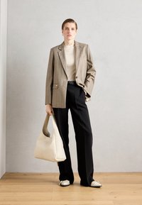 Beige Karo-Blazer mit einem einzigen Knopf, cremefarbenem Ripp-Pullover, schwarzen Hosen, weißer Tasche und gemusterten Schuhen auf einem Holzboden.