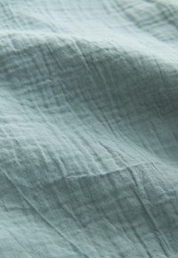 Puha, világoskék szövet finom gyűrődésekkel és texturált, szövött mintával természetes fényben.