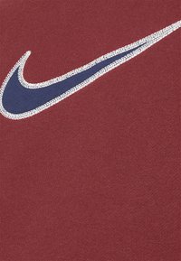 Bordeaux mikina s námořnickým logem Nike ohraničeným stříbrným šitím na texturované tkanině. Bohatá barva s hladkým povrchem.