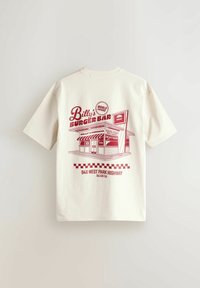 Camiseta de algodón crema con un gráfico rojo de "Billy's Burger Bar" que muestra una ilustración de un diner y un borde en cuadros.