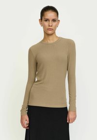 Bézs színű, hosszú ujjú, bordázott anyagból k�észült felső, kerek nyakkivágással, testhezálló fazonnal és sima tapintással, fekete szoknyával párosítva.