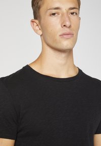 Černé krátké tričko s krátkým rukávem vyrobené z texturované tkaniny, s kulatým výstřihem a volným střihem.