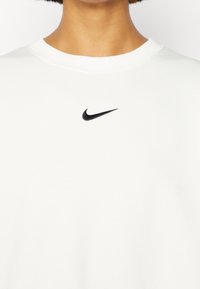 Vit sweatshirt i mjukt tyg med en liten svart Nike-swoosh logo på bröstet. Rund hals och ribbade muddar.
