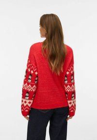Roter Pullover mit Schneemannmuster auf weißen und roten gestrickten Ärmeln, lockere Passform und weiche Textur, kombiniert mit dunkelblauen Jeans.