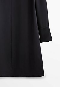 Vêtement noir à manches longues avec un large poignet et un ourlet droit, présenté sur un fond blanc uni.