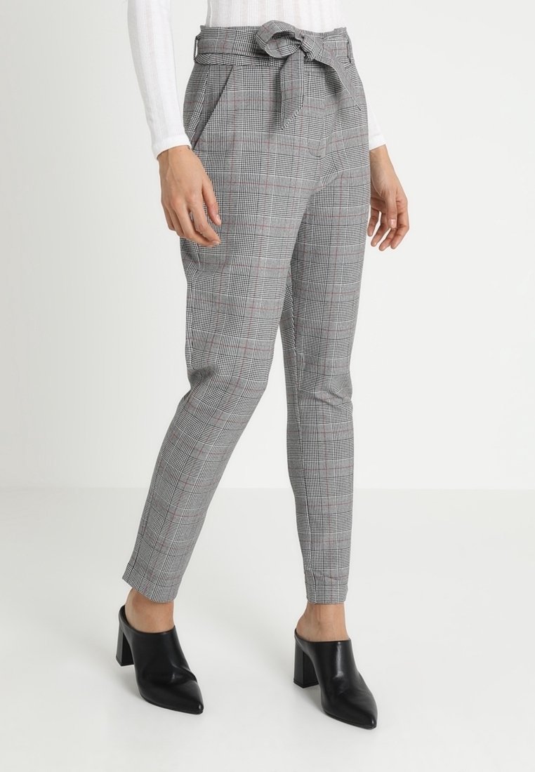 Pantalons gris à carreaux avec une ceinture et un détail de cravate, affichant une coupe slim et une longueur jusqu'à la cheville, associés à des mules noires à talons blocs.