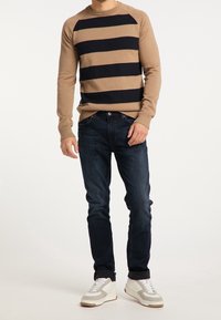 Sweter w brązowe paski z granatowymi poziomymi pasami, zestawiony z ciemnoniebieskimi dżinsami i białymi trampkami z szarymi akcentami i podeszwą.