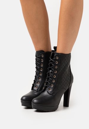 Botines negros de tacón alto con detalles texturizados, que presentan ojales metálicos, cordones delanteros y un acabado liso similar al cuero.