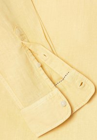 Manche de chemise en lin jaune avec poignet boutonné et une patte recouvrant une boutonnière cousue.