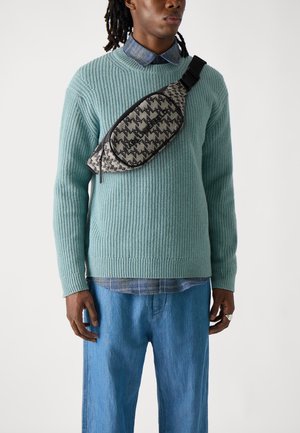 Light blue ribbed knit sweater, casual blue check shirt underneath, paired with loose denim pants. Black and beige patterned sling bag across torso.