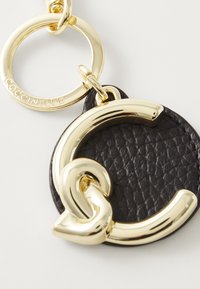 Black leather keychain featuring a shiny gold logo accent. The design includes a textured circular tag and a round attachment ring.