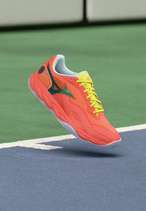 Chaussure de course orange vif avec des lacets jaunes et un logo vert flottant au-dessus d'une surface de court de tennis bleue et verte.