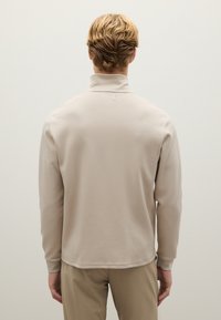 Suéter beige con cuello alto, textura suave y mangas largas. Diseño simple con dobladillo recto, vista desde la parte posterior.