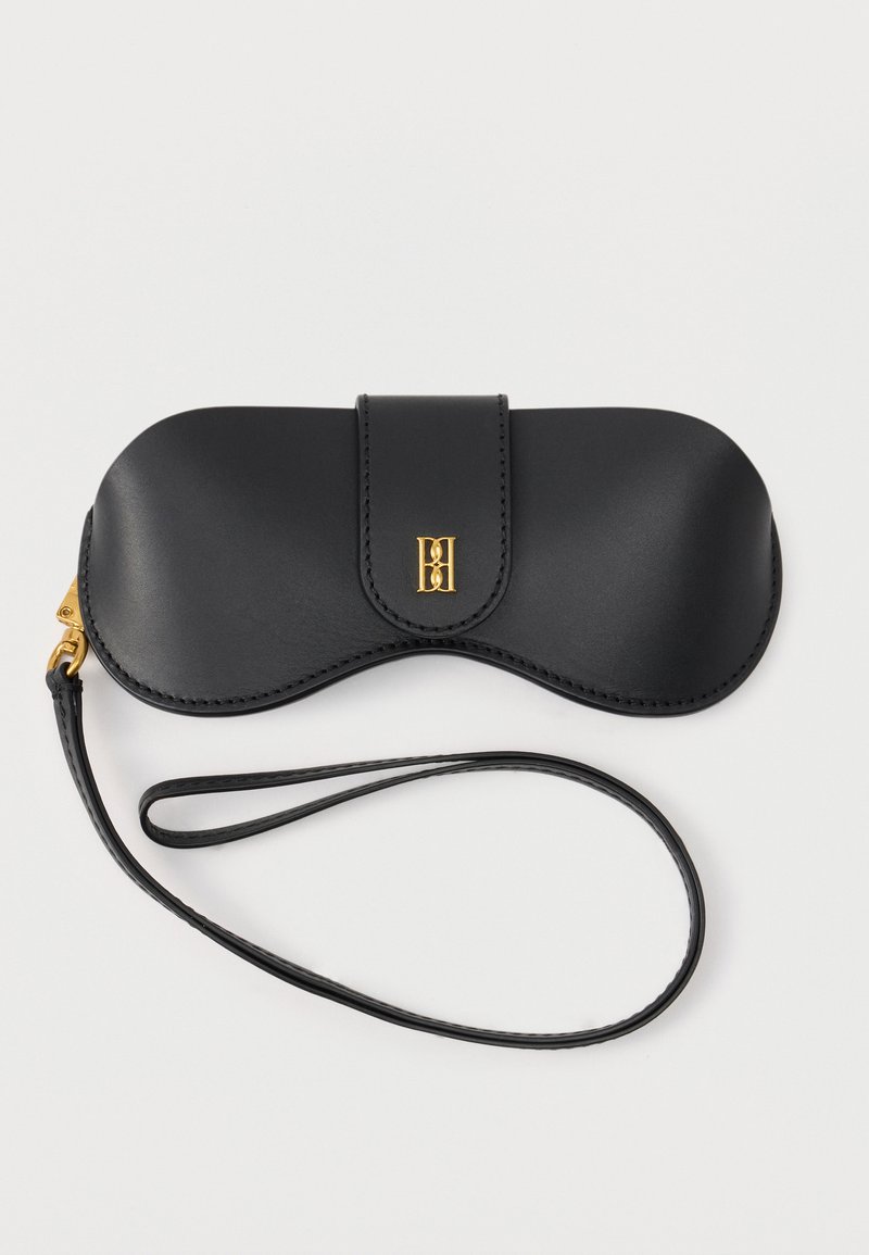 Μαύρη θήκη γυαλιών από δέρμα με καπάκι, χρυσή αγκράφα και λουράκι καρπού σε λευκό φόντο.