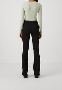 Ljusgrön ribbad långärmad topp tillsammans med högmidjade svarta utsvängda byxor, som visar upp en välsittande silhuett och slät textur.