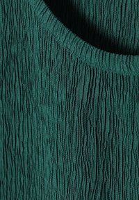 Teal textuurstof top met een golvende oppervlakte, ronde halslijn en zachte afwerking, die verticale strepen en een subtiel patroon benadrukt.