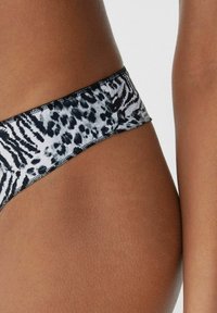 Czarny i biały kostium bikini w stylu wzorzystym, z niskim stanem, charakteryzujący się gładką teksturą i kontrastowym wykończeniem szwami wzdłuż pasa.