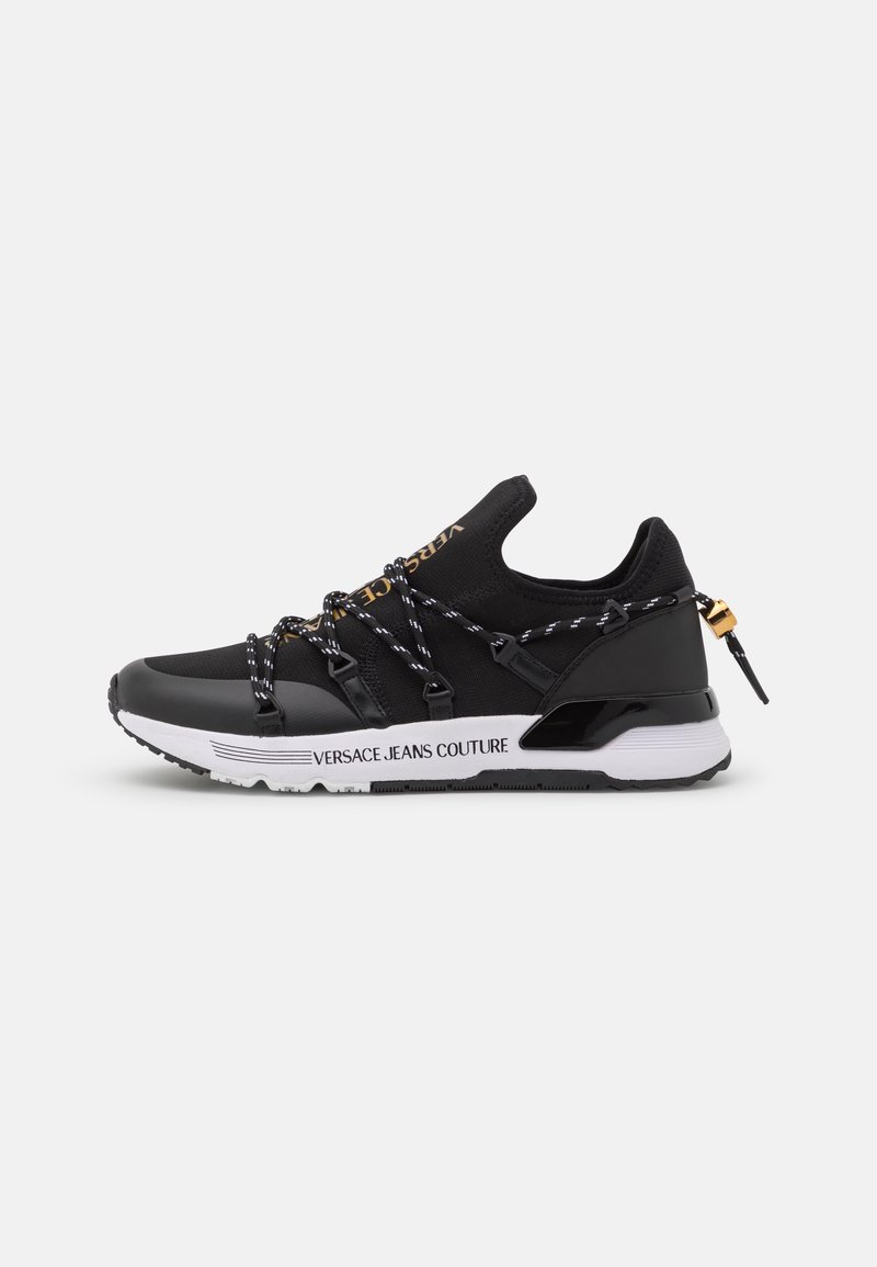Baskets noires avec semelle en caoutchouc, tige en textile, lacets décoratifs et un accent doré. Logo "VERSACE JEANS COUTURE" sur le côté.