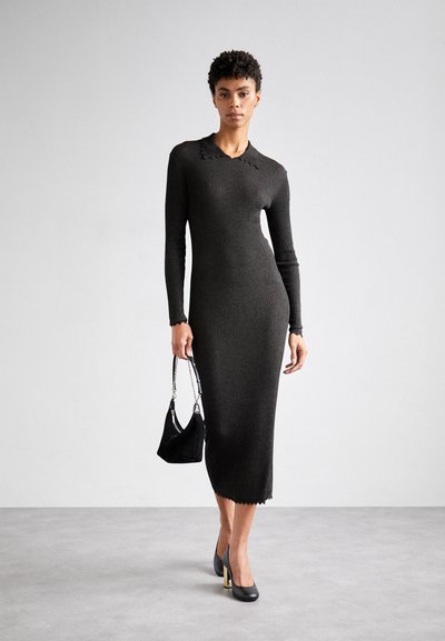 Abito nero a maniche lunghe, in maglia a coste, con scollatura a forma di onde, silhouette aderente e lunghezza fino al polpaccio. La modella tiene una piccola borsa nera.