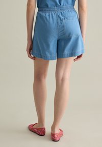 Shorts in denim azzurro chiaro con vita elastica, una tasca posteriore e orlo che termina appena sopra la coscia. Abbinati a ballerine rosse con motivo.