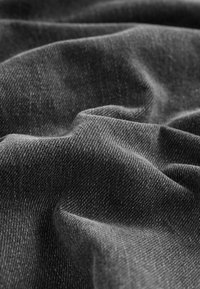 Gros plan sur un tissu en denim gris foncé froissé montrant la texture et le motif de tissage.