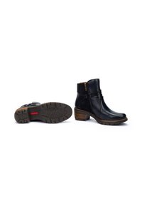 Botas de tobillo de piel negra con cierre de cremallera, acentos laterales texturizados y un tacón apilado. Suela de goma con un patrón de relieve.