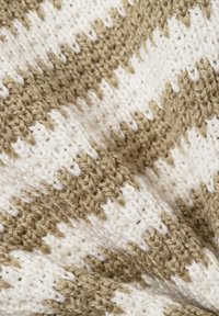 Strickdecke mit einem beige-weißen Zickzackmuster, aus weichem Garn mit einer strukturierten Oberfläche, die hervorgehobene Stiche zeigt.
