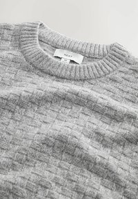 Suéter gris texturizado con un patrón de cuadros tejido, cuello acanalado y una etiqueta que indica la talla M.