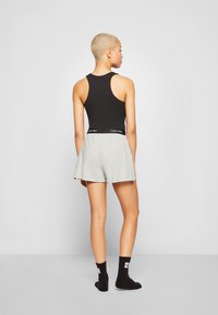 Camiseta sin mangas negra con pantalones cortos grises que presentan una cinturilla elástica. Usado con calcetines negros que muestran un logo. Textura de tela suave.