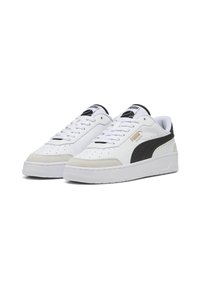 White sneakers with black accents and gold logo, featuring a smooth leather upper, perforated toe, and a textured rubber sole.