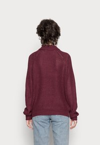 Pull en maille bordeaux à coupe relax, avec un ourlet et un col côtelés. Doté de manches longues avec un léger plissé aux poignets.