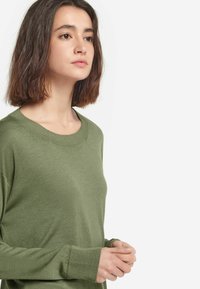 Zielony sweter z dzianiny z okrągłym dekoltem i prążkowanymi mankietami, o luźnym kroju i gładkiej fakturze.