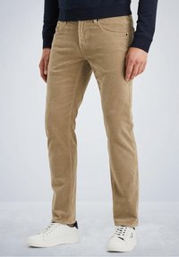 Beige corduroy broek met een rechte pasvorm, voorzien van vijf zakken en subtiele stiksels. Gecombineerd met witte sneakers en een donkere top.