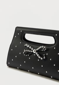 Μαύρη τσάντα χεριού από λεία ύλη, διακοσμημένη με μικρές ασημένιες πέρλες. Περιλαμβάνει μια διακοσμητική κορδέλα και ένα σχέδιο χερούλι με κοπή.