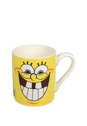 Tazza in ceramica gialla con un grande volto sorridente da cartone animato con occhi blu, denti grandi e un manico bianco curvo.