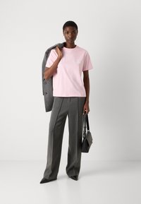 Pink cotton t-shirt with short sleeves, paired with gray tailored trousers, and a gray blazer draped over the shoulder. Black handbag.