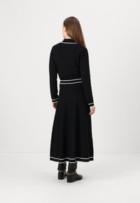 Black knit dress with a fitted top and flared skirt. Features white trim at the collar, waist, and hem. Worn with black boots.