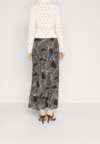 Top lungo a maniche in pizzo bianco con motivo a diamante abbinato a una gonna maxi nera con disegni di linee bianche ondulate; sandali neri con tacco alto.