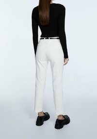 Suéter corto de manga larga de color negro con un diseño de cinta, combinado con pantalones ajustados blancos. El calzado tiene suelas negras gruesas. Diseño simple sin patrones.