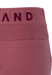 Dehnbare pinke Jogginghosen verfügen über einen gerippten Bund mit dunkelroter Schrift und einer Tasche auf der Rückseite, mit einer insgesamt glatten Textur.