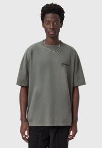 Camiseta de gran tamaño en gris claro con cuello redondo, mangas cortas y pequeño logo negro "ALLSAINTS" en el pecho. Textura de algodón suave.