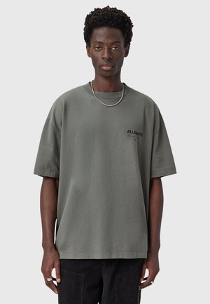 T-shirt oversized gris clair avec un col rond, des manches courtes et un petit logo noir "ALLSAINTS" sur la poitrine. Texture en coton lisse.