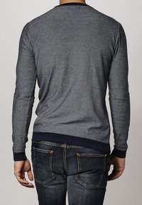 Grijze gebreide trui met een gestructureerd uiterlijk, ronde halslijn en marineblauwe geribde manchetten en zoom, gecombineerd met donkerdenim jeans.