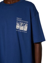 Osoba nosząca niebieską koszulkę z białym tekstem i grafiką mapy z napisem "HALO 196819721981" oraz "HIGH ALTITUDE LOW OPENING."