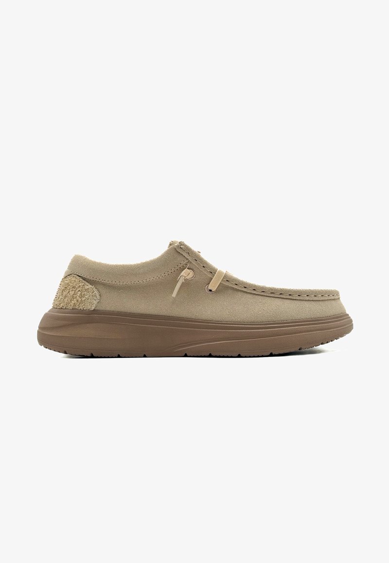 Scarpe slip-on beige con una trama simile alla pelle scamosciata, dotate di un tacco accentato color cammello, dettagli cuciti e una suola in gomma flessibile.